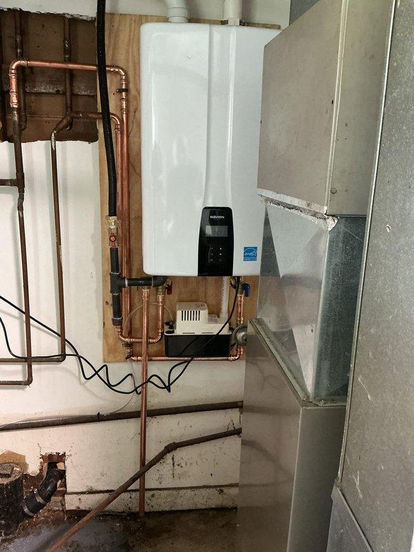 Completed installation of wall-mounted tankless water heater system in basement utility room. Removed existing water heating equipment and installed new Energy Star certified tankless unit on plywood backing board mounted to concrete block wall. Configured comprehensive copper piping network including supply and return lines with appropriate shut-off valves, pressure relief connections, and gas line integration. Installed condensate pump for drainage management and connected venting ductwork through galvanized steel exhaust system. Routed electrical supply with proper conduit and established digital control panel programming. All connections pressure tested and system commissioned to manufacturer specifications.