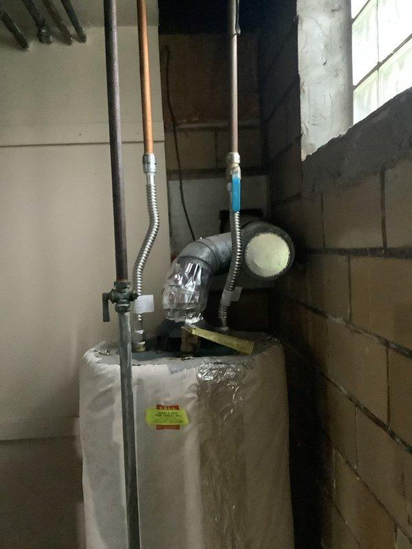 Responded to service call for gas water heater with home gas supply shut off due to existing gas leak. Performed visual inspection of tanked water heater unit of unknown age located in basement utility area. Assessed condition of unit, gas supply lines, water connections, venting system, and associated plumbing components including copper piping, flexible connectors, and shut-off valves. Documented equipment configuration with circulator pump mounted on top of water heater and standard plumbing connections. Provided estimate for gas leak repair and potential water heater replacement options.