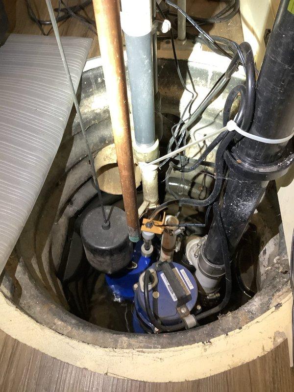 Responded to sump pump issue at a twenty-year-old residential property where the original system was previously installed. Upon arrival, performed comprehensive inspection of the dual-pump battery backup sump pump system, which included a primary pump (ST103-GL model) and backup pump configuration. Evaluated all plumbing connections including the main PVC discharge piping, check valves (SPC-250 GT), V-pipe assembly, 45-degree elbows, no-hub couplings, and pipe adapters. Inspected the backup double float switch mechanism and verified proper cable tie mounting to couplings. Examined the concrete sump pit for structural integrity and assessed water levels at the pump base. Checked all electrical connections, including the backup battery system wiring and float switch cables. Verified proper operation of both primary and backup pumps, tested check valve functionality to prevent backflow, and confirmed secure mounting of all pipe brackets and clamps. Documented the complete system configura