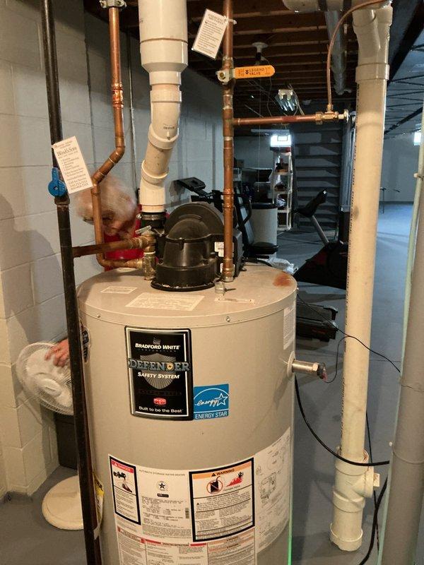 Responded to service call for failed hot water tank in 22-year-old residential property. Upon arrival, assessed existing water heater system and confirmed unit was no longer operational. Proceeded with complete water heater replacement, installing new Bradford White Defender Safety System unit with Energy Star certification. 

Connected all copper supply and discharge piping with proper fittings and joints. Installed pressure relief valve and safety components per manufacturer specifications. Integrated white PVC venting system to exterior wall, ensuring proper combustion air intake and exhaust ventilation. Installed blue shut-off valve on cold water supply line for future serviceability. Verified all connections for proper sealing and tested system for leaks.

Mounted electrical components and verified proper grounding. Ensured adequate clearances around unit per code requirements. System tested and confirmed operational with proper hot water delivery throughout residence.