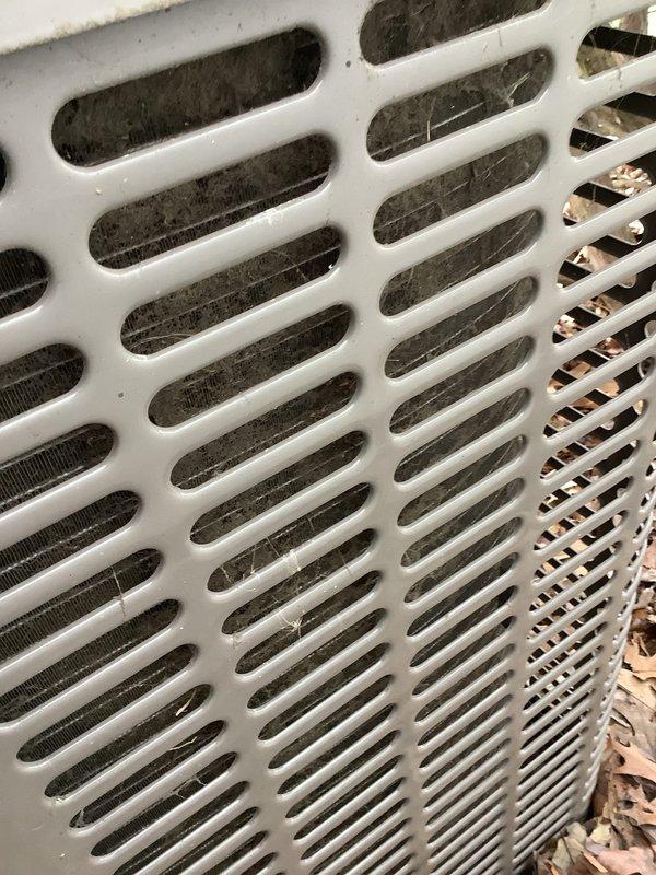 Completed preventative maintenance tune-ups on two outdoor condensing units at residential property. The older unit on the left showed significant vegetation encroachment with plant growth penetrating the protective grille and heavy debris accumulation on condenser coils, while the newer cylindrical unit on the right was in better overall condition with less environmental impact. Performed standard maintenance procedures including cleaning condenser coils, removing organic debris from both units, and clearing vegetation from around equipment to ensure proper airflow and system efficiency.