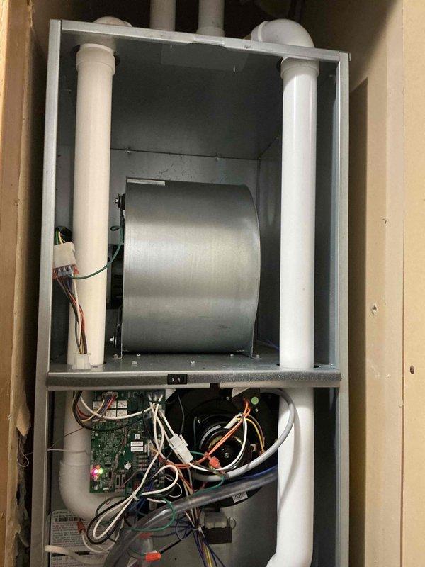 Responded to service call for non-operational central air conditioning system. Conducted comprehensive assessment of existing HVAC installation, which included a wall-mounted air handler unit with integrated blower assembly, heat exchanger components, and control board system. Documented current equipment configuration showing horizontal blower motor installation, dual PVC venting system, electronic control board with multiple wire harnesses, and complete mechanical component layout within framed wall cavity. Photographed interior components including cylindrical heat exchanger, circuit board connections, wire routing, and overall system installation for estimate preparation. Provided detailed equipment evaluation and replacement recommendations based on current system condition and operational failure.