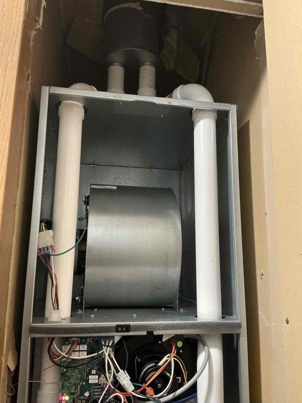Responded to service call for non-operational central air conditioning system. Conducted comprehensive assessment of existing HVAC installation, which included a wall-mounted air handler unit with integrated blower assembly, heat exchanger components, and control board system. Documented current equipment configuration showing horizontal blower motor installation, dual PVC venting system, electronic control board with multiple wire harnesses, and complete mechanical component layout within framed wall cavity. Photographed interior components including cylindrical heat exchanger, circuit board connections, wire routing, and overall system installation for estimate preparation. Provided detailed equipment evaluation and replacement recommendations based on current system condition and operational failure.