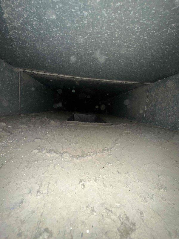 Completed comprehensive duct cleaning service with photographic documentation of system condition. Inspection revealed significant accumulation of dust and debris throughout the ventilation system, including thick sediment buildup on duct floors and particulate matter coating interior surfaces. Metal ductwork showed evidence of age-related deterioration with visible discoloration and weathering patterns. Cleaned rectangular supply or return trunk lines with heavy dust deposits on both horizontal and vertical surfaces. Accessed crawl space areas where wooden structural components exhibited moisture-related staining and contamination within floor joist cavities. Performed cleaning procedures to remove accumulated debris from accessible duct sections and documented pre-existing conditions including potential moisture intrusion issues in structural spaces adjacent to ductwork.
