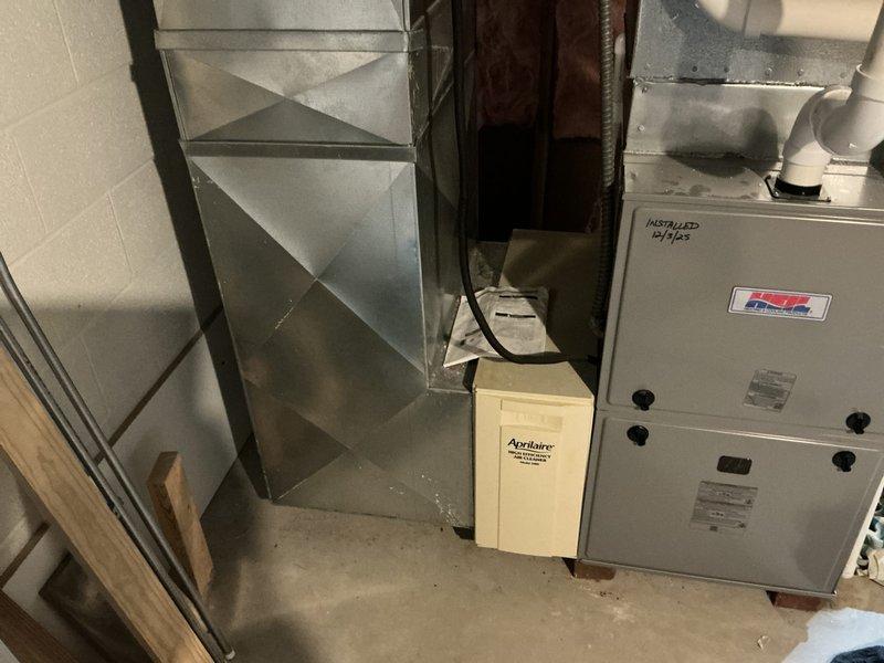 Completed HVAC system estimate for replacement of existing furnace unit installed in October 2003, as indicated by handwritten notation on ductwork. Assessed beige/tan gas furnace with connected white PVC venting pipes and galvanized sheet metal supply ductwork in unfinished basement utility area. Documented current equipment configuration including manufacturer specifications, system age verification, and existing ductwork layout to provide replacement options excluding builder-grade equipment exceeding specified budget parameters.