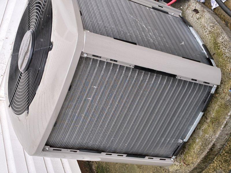 Completed MVP cooling maintenance visit on outdoor heat pump unit. Inspected condenser coils and found moderate dirt and debris accumulation on aluminum fins, particularly in upper and middle sections. Observed minor oxidation on refrigerant line connections. Photographed unit condition showing typical seasonal weathering on exterior components and documented coil cleanliness for maintenance records. Unit operational at time of inspection with fan assembly and heat exchanger accessible for routine service.