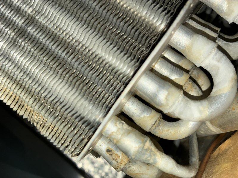 Completed MVP cooling maintenance visit on outdoor heat pump unit. Inspected condenser coils and found moderate dirt and debris accumulation on aluminum fins, particularly in upper and middle sections. Observed minor oxidation on refrigerant line connections. Photographed unit condition showing typical seasonal weathering on exterior components and documented coil cleanliness for maintenance records. Unit operational at time of inspection with fan assembly and heat exchanger accessible for routine service.