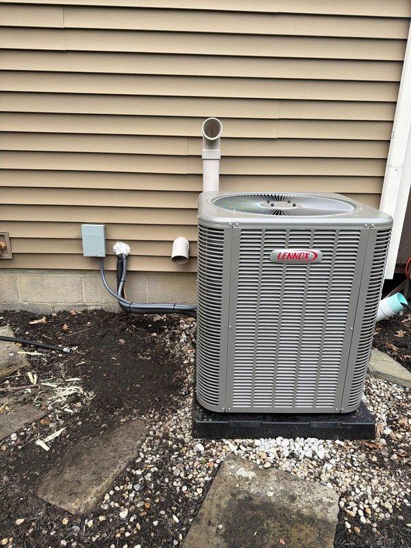 Completed installation of a 90% efficiency furnace, air conditioning system, and humidifier as a complete HVAC system replacement. Installed new Lennox outdoor condensing unit on rubber isolation pad with white stone base for proper drainage and vibration dampening. Mounted electrical disconnect box on exterior wall with appropriate conduit and wiring connections. Replaced fuse block assembly with new Littelfuse LNH 30 amp fuses to ensure proper electrical protection for the system. Ran PVC condensate drain line vertically along exterior wall for proper moisture removal. All equipment positioned for optimal airflow clearance and serviceability. System tested and verified operational upon completion.