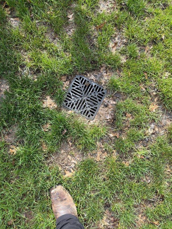 Responded to service call for clogged yard drainage system. Conducted on-site assessment of existing drainage infrastructure, including inspection of downspout discharge point at building foundation and in-ground storm drain grate in lawn area. Documented current conditions through photographic evidence showing debris accumulation around downspout base and storm drain location. Provided professional quote for installation of French drain system to improve yard drainage and prevent water pooling issues near foundation.