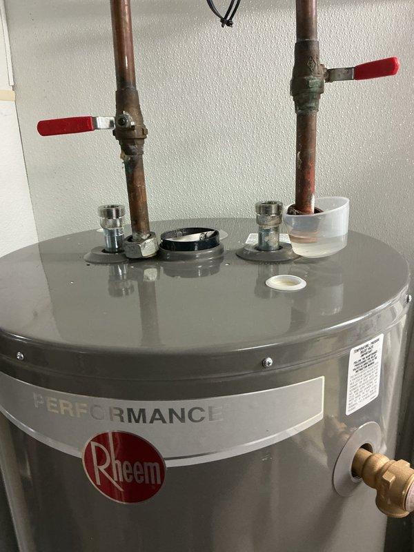 Completed water line installation and connection to Rheem Performance tanked water heater. Connected hot and cold water supply lines using copper piping with shut-off valves featuring red handles installed at the top of the unit for proper water flow control and future maintenance access. All connections were secured with threaded fittings and compression nuts to ensure leak-free operation, and the unit was verified to be properly positioned and ready for service.