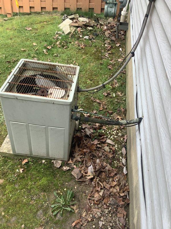 Provided estimate for replacement of 1990's era residential air conditioning system utilizing obsolete R22 refrigerant. Existing outdoor condenser unit shows significant age-related wear and deterioration with accumulated debris on fan grill and weathered exterior casing. Indoor air handler located in garage attic space accessed via ceiling panel. Due to phaseout of R22 refrigerant and age of equipment exceeding typical service life, recommended complete system replacement with modern high-efficiency unit using current refrigerant technology.