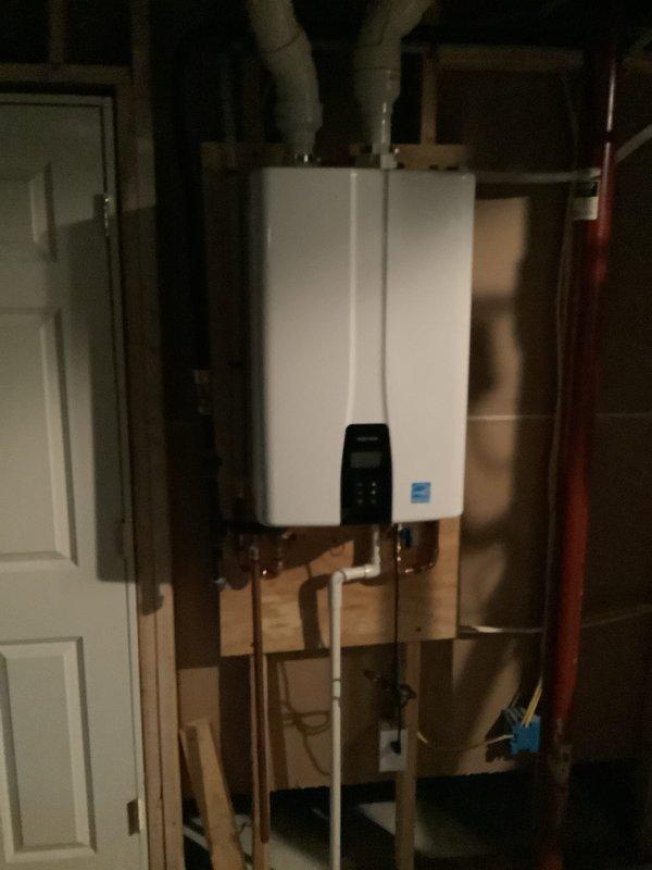 Removed two existing power vent water heater units, expansion tank, and drain pan from the utility area. Installed new Navien tankless water heater system with complete connection of gas supply lines, copper water piping with brass fittings, electrical service, and venting through existing infrastructure. All components properly mounted to wooden framing, system tested and verified operational with Energy Star certified unit displaying normal function on digital interface.