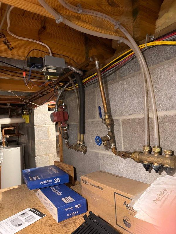 Responded to service call for leaking water heater in residential basement. Upon inspection, confirmed 16-year-old tanked water heater was leaking from bottom of unit, indicating internal tank failure typical for units beyond expected service life. Documented existing installation including copper supply lines, brass fittings, expansion tank, and connections to home plumbing system. Photographed equipment configuration showing water heater positioned adjacent to HVAC system with exposed ceiling joists and utility piping. Provided assessment and recommendations for water heater replacement due to age and condition of unit.