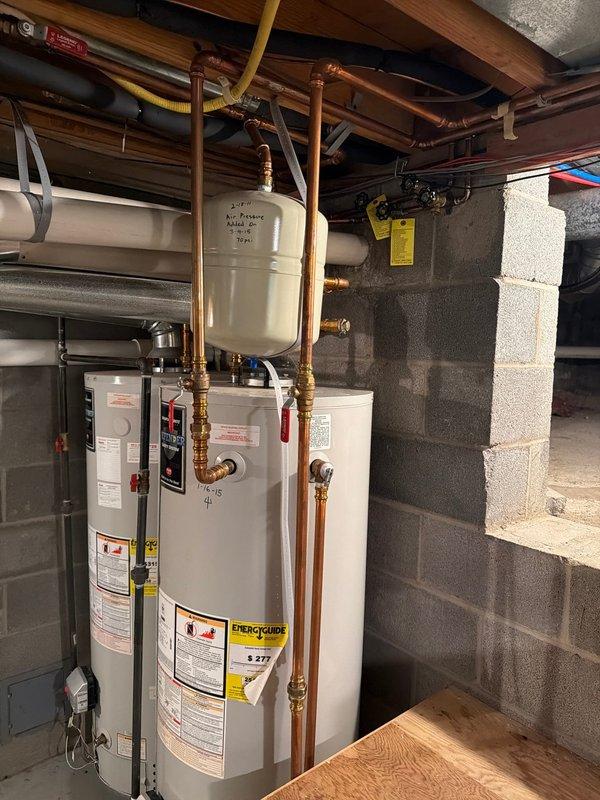 Responded to service call for leaking water heater in residential basement. Upon inspection, confirmed 16-year-old tanked water heater was leaking from bottom of unit, indicating internal tank failure typical for units beyond expected service life. Documented existing installation including copper supply lines, brass fittings, expansion tank, and connections to home plumbing system. Photographed equipment configuration showing water heater positioned adjacent to HVAC system with exposed ceiling joists and utility piping. Provided assessment and recommendations for water heater replacement due to age and condition of unit.