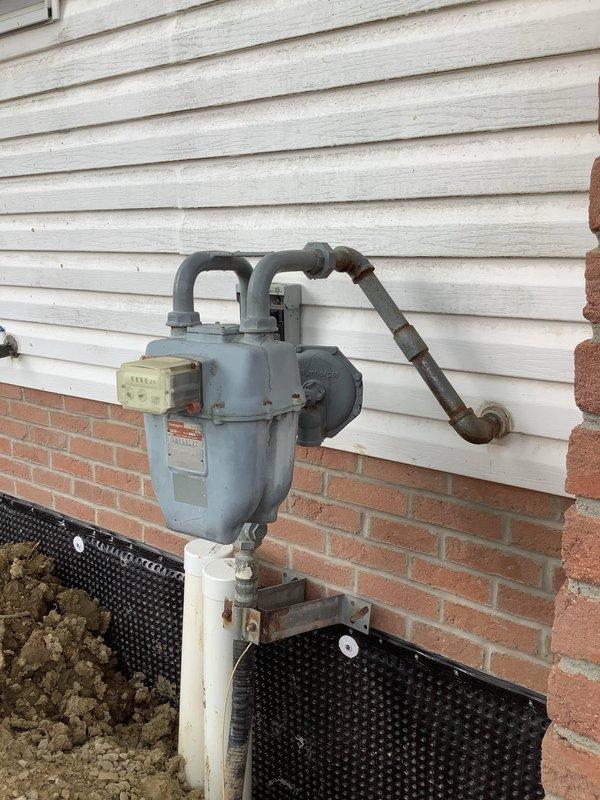 Responded to service call for gas meter that was removed during wall maintenance and became twisted during reinstallation. Upon arrival, assessed the exterior-mounted natural gas meter installation and confirmed the meter assembly had been improperly repositioned. Carefully untwisted the gas meter piping to restore proper alignment and orientation of the meter body and connecting lines. Reattached and secured the meter assembly to the exterior wall mounting bracket, ensuring all pipe connections were properly aligned with both the building supply lines and the curved riser pipes. Verified all connections were secure and the meter was level and stable on its mounting stand. Inspected the complete installation including the horizontal supply piping and vertical connections to confirm proper positioning and no stress on joints or fittings.