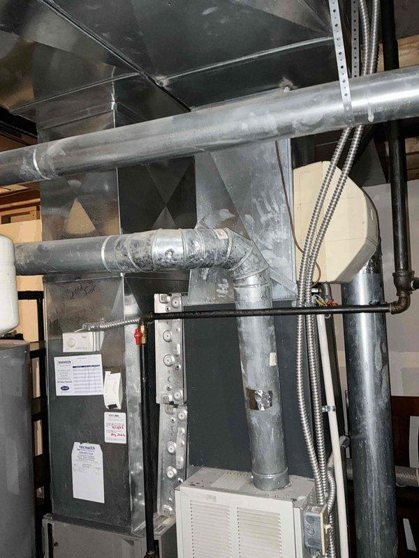 Completed comprehensive HVAC system replacement estimate for dual furnace and air conditioning units under buy-one-get-one promotion. Assessed existing basement installation including current air handling unit, galvanized ductwork configuration, and electrical connections. Documented existing system components through detailed photography showing furnace with exposed burner assembly, copper tubing, associated ductwork including horizontal and vertical runs with elbow joints, and flexible metal conduits for electrical and gas lines. Evaluated mechanical room setup for replacement feasibility and provided customer with equipment options and installation specifications for two complete HVAC systems.