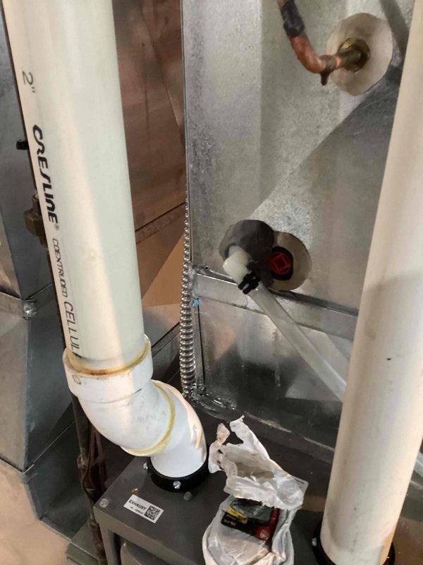 Responded to AC leak at condensate drain line near furnace. Inspected white PVC condensate piping system and identified leak at pipe joint connection showing water staining and discoloration. Repaired defective connection, tested system operation, and verified proper drainage with no further leakage detected.