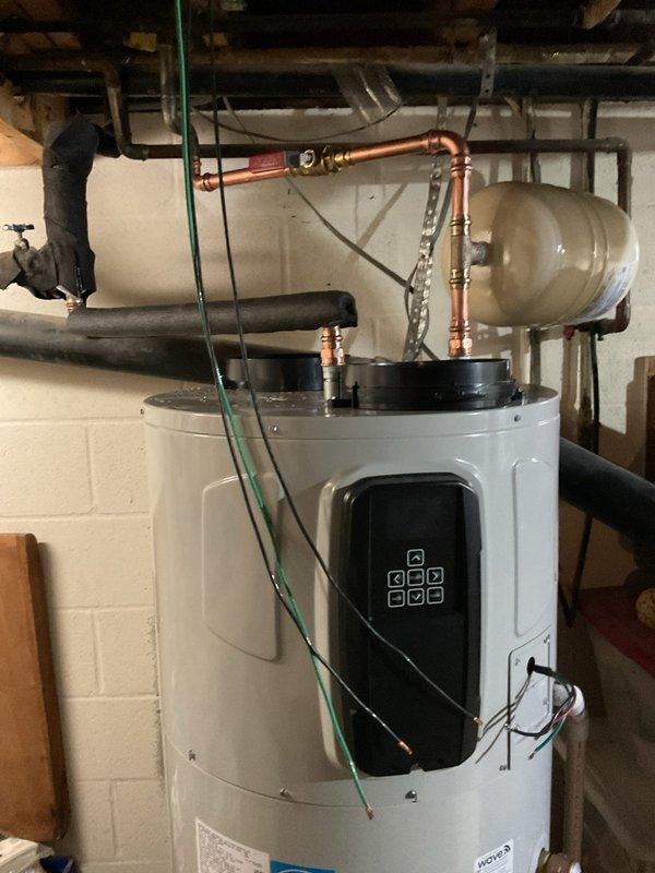 Completed installation of a 50-gallon Bradford White Aerotherm heat pump water heater in residential basement utility area. Staged incoming water heater kit with parts, performed copper pipe connections with soldered joints and compression fittings at top of unit, and installed expansion tank with mounting bracket. Reworked electrical wiring to accommodate new heat pump water heater system, connecting power supply and configuring digital control panel for operation.