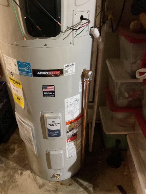 Completed installation of a 50-gallon Bradford White Aerotherm heat pump water heater in residential basement utility area. Staged incoming water heater kit with parts, performed copper pipe connections with soldered joints and compression fittings at top of unit, and installed expansion tank with mounting bracket. Reworked electrical wiring to accommodate new heat pump water heater system, connecting power supply and configuring digital control panel for operation.