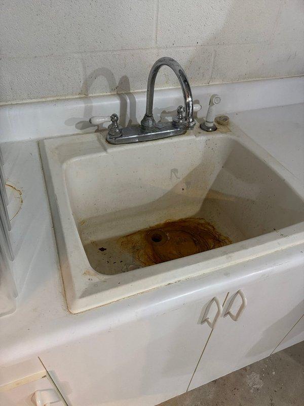 Responded to service call for multiple faucet installations and plumbing fixture work. Installed chrome utility sink faucet with dual handles and arched spout on white basin in utility area, addressing existing rust staining and drainage concerns. Serviced bathtub faucet assembly and spout in bathroom with cream-colored fiberglass surround, resolving reported leak issue. Documented existing mineral deposits and surface staining on fixtures for customer awareness.