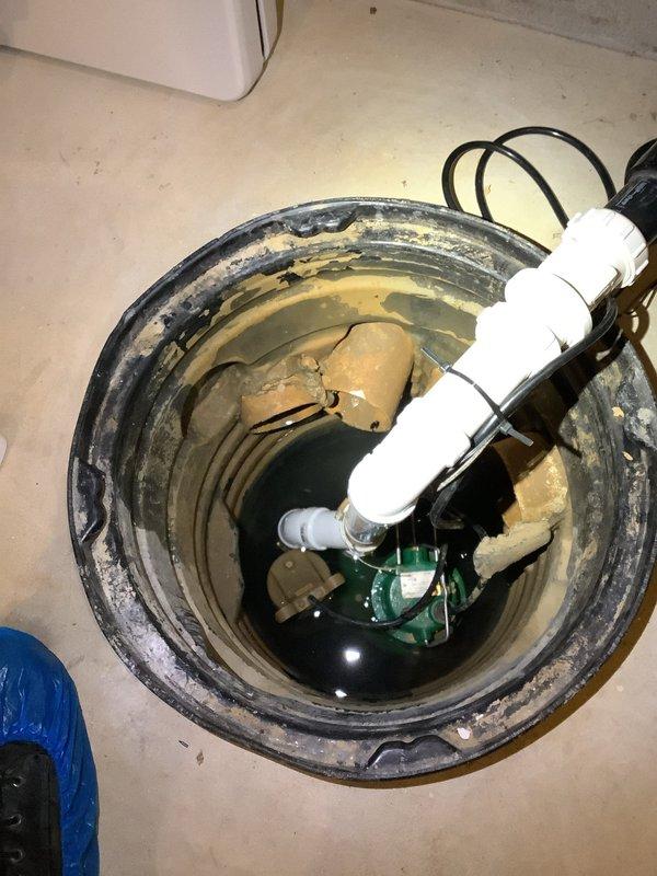 Responded to service call for dual sump pump system experiencing operational issues. Upon arrival, assessed both primary and backup sump pumps in basement pit. Primary pump, approximately one year old, was creating air bubbles at end of discharge cycle indicating improper installation or venting issues. Backup pump, approximately seven years old, had failed and was not discharging water when activated. 

Inspected sump pit configuration and found water accumulation with visible sediment buildup along interior walls. Examined discharge piping system including vertical PVC pipe and associated fittings for blockages or improper connections. Evaluated electrical connections and float switch mechanisms on both pump units. Documented existing installation with photographs showing pump components, pit condition, and piping arrangement for assessment and future reference.