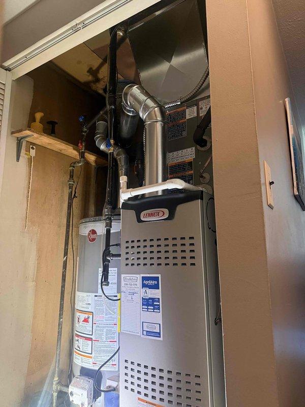 # HVAC Install - Complete System

Completed installation of 80-foot AC lineset routed through attic space to connect outdoor condensing unit to indoor air handler. Installed Lennox furnace system in utility closet with proper ductwork connections, including flexible metal ducting and silver-colored supply/return plenums with elbow joints for optimal airflow distribution. System positioned adjacent to existing Rheem water heater with adequate clearance for service access and ventilation requirements. All refrigerant lines properly insulated and secured throughout attic run to prevent energy loss and ensure efficient operation. Electrical connections completed per manufacturer specifications and local code requirements. Verified all mechanical connections, tested system operation, and confirmed proper airflow through ductwork. Installation includes all necessary labels, warning stickers, and specification documentation affixed to equipment. System commissioned and ready for operation.