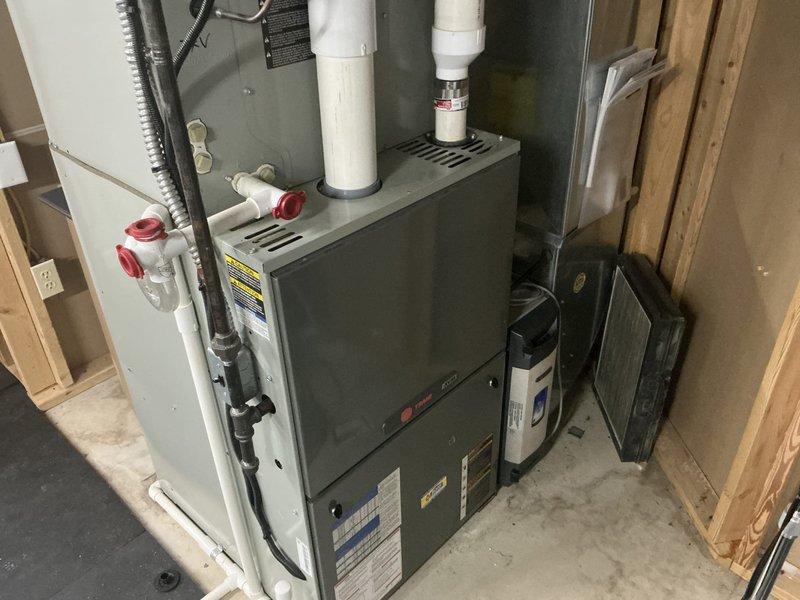 Completed comprehensive assessment of existing residential HVAC system for replacement estimate on large home exceeding 3000 square feet. Evaluated current basement-installed natural gas furnace with associated PVC venting, condensate drainage system, and electrical connections, as well as outdoor Trane air conditioning unit positioned on concrete pad against building exterior. Documented equipment specifications, installation configuration, and spatial requirements to provide accurate replacement recommendations for complete heating and cooling system upgrade.