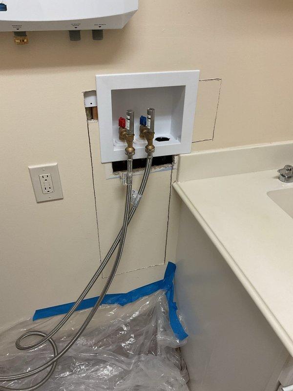 Opened wall to access existing washer box and replaced it with a similar recessed outlet box model. Installed new brass shut-off valves with dual hot and cold water connections and connected flexible stainless steel braided supply lines. Protected work area with plastic sheeting and painter's tape throughout the installation process.