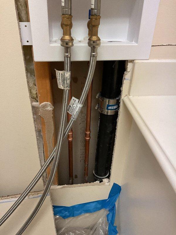 Opened wall to access existing washer box and replaced it with a similar recessed outlet box model. Installed new brass shut-off valves with dual hot and cold water connections and connected flexible stainless steel braided supply lines. Protected work area with plastic sheeting and painter's tape throughout the installation process.