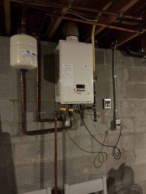Responded to service call for inefficient Verne brand tanked water heater at 32-year-old residential property. Upon inspection, determined existing tank-style unit had reached end of service life and recommended replacement with high-efficiency tankless system. Removed old tanked water heater and installed new Rinnai tankless water heating unit on basement wall with proper clearances and ventilation. Connected copper supply lines, installed expansion tank with isolation valves, and ran new gas line to unit. Mounted exterior PVC vent termination through foundation wall above grade with appropriate flashing and weather protection. Installed electrical service and control panel with indicator lights. Tested all connections for leaks, verified proper gas pressure, commissioned unit according to manufacturer specifications, and confirmed hot water delivery throughout home. System operating at optimal efficiency with significant energy savings compared to previous tank-style heater.