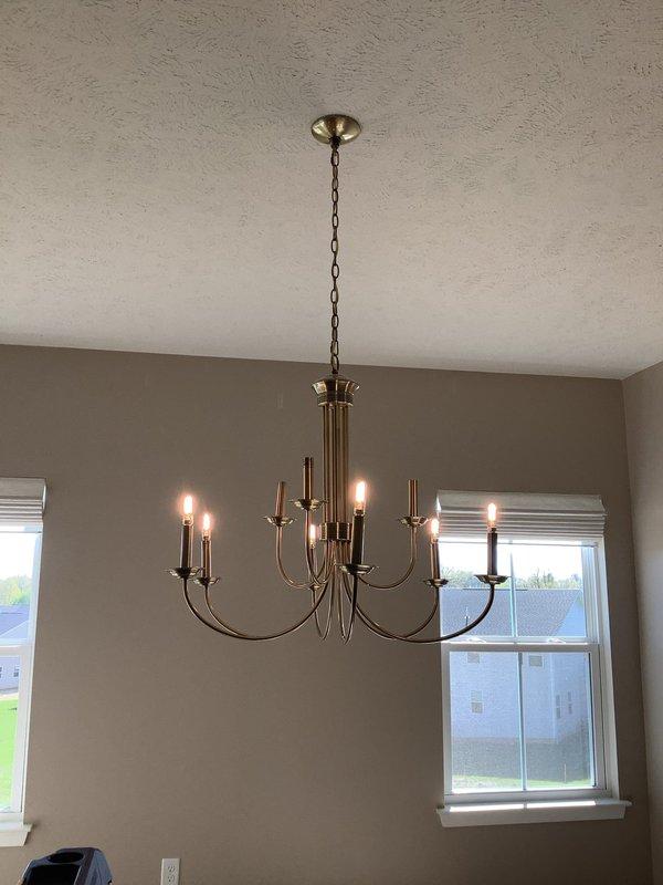 Replaced existing chandelier with a six-arm brushed nickel fixture featuring candle-style bulbs in residential room. Installed ceiling fan with integrated light fixture and dark wooden blades into builder-wired junction box in separate room, ensuring proper mounting and electrical connections for both fixtures.