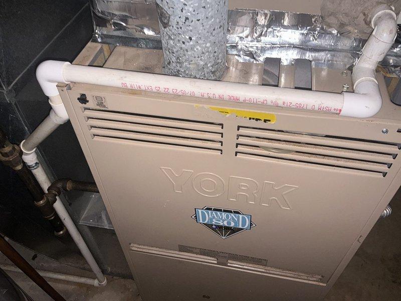 Completed furnace replacement estimate for residential HVAC system. Evaluated existing York Diamond 80 furnace installation in basement utility area, documented current equipment configuration including PVC venting connections, ductwork interface, and proximity to water heating equipment. Photographed unit specifications, ventilation components, and mechanical room layout to provide comprehensive assessment for replacement options.