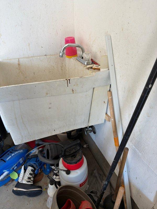 Responded to service call for plumbing fixture leak in utility area of 36-year-old home. Upon inspection, identified active leak at chrome faucet spout on wall-mounted utility sink. Customer had temporarily placed plastic cup over spout to contain dripping water. Assessed supply line connections and shutoff valves beneath sink, noting age-appropriate wear on metal braided supply hoses and wall-mounted angle stops with round handles. Tightened faucet connections, replaced worn washers, and tested for proper water flow and complete shutoff. Verified all supply line connections were secure with no additional leaks present. System restored to full functionality with no further dripping observed.