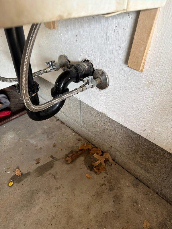Responded to service call for plumbing fixture leak in utility area of 36-year-old home. Upon inspection, identified active leak at chrome faucet spout on wall-mounted utility sink. Customer had temporarily placed plastic cup over spout to contain dripping water. Assessed supply line connections and shutoff valves beneath sink, noting age-appropriate wear on metal braided supply hoses and wall-mounted angle stops with round handles. Tightened faucet connections, replaced worn washers, and tested for proper water flow and complete shutoff. Verified all supply line connections were secure with no additional leaks present. System restored to full functionality with no further dripping observed.