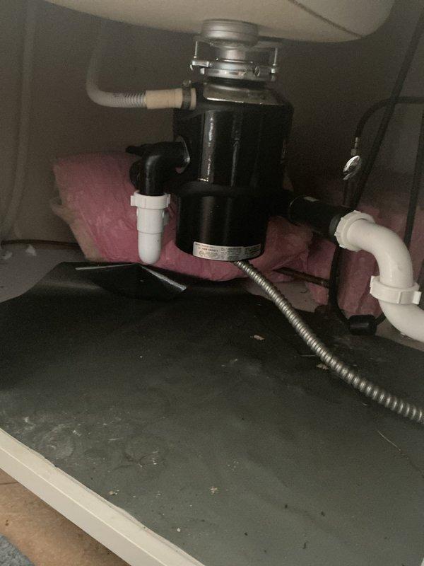 Performed tanked water heater flush to remove sediment buildup and maintain unit efficiency in 27-year-old home. Diagnosed malfunctioning garbage disposal unit that hummed but failed to operate; assessed disposal motor and mounting assembly under kitchen sink for potential jam or electrical failure. Documented existing plumbing configuration including disposal unit, PVC drainage system, and electrical connections via photographs for service records.