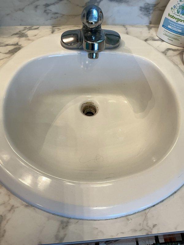 Responded to service call for plumbing fixture estimate. Assessed existing bathroom fixtures including a chrome-plated shower/tub control valve with single lever handle, a white ceramic oval drop-in sink with three-handle chrome faucet set in marble countertop, and toilet requiring replacement. Photographed current fixtures and documented conditions to provide accurate estimate for complete bathroom fixture replacement including new sink, toilet, and shower control valve assembly.