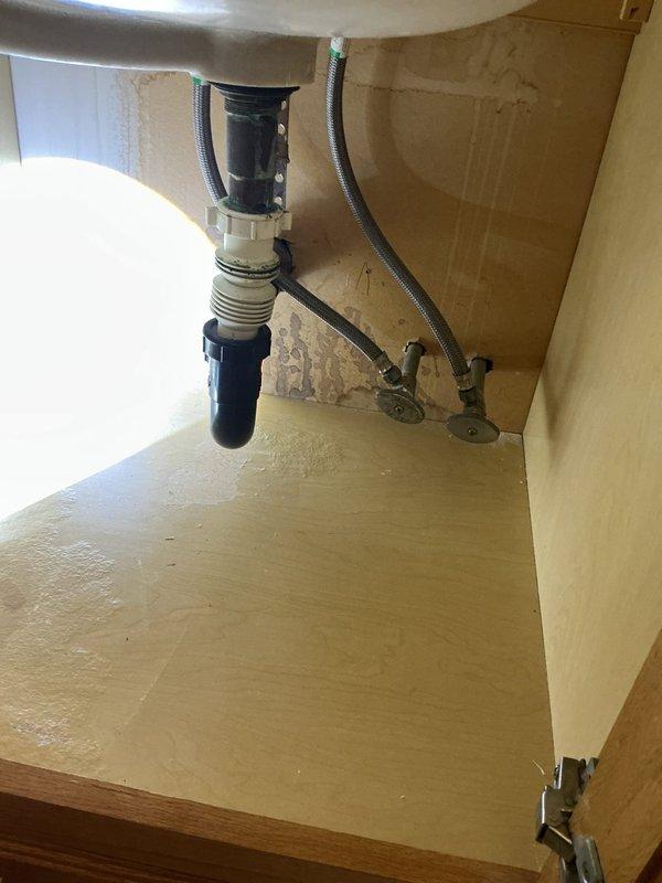 Responded to service call for leaky bathroom sink on main level. Upon inspection, identified water leak originating from supply line connection beneath sink cabinet. Examined P-trap assembly, flexible braided supply lines, and shutoff valves - all connections appeared intact at cabinet level. Further investigation revealed leak had migrated through ceiling below, causing significant water damage with peeling paint and exposed plaster in adjacent room. Tightened supply line connections, tested system under pressure, and verified no active leaking at source. Documented existing water damage to ceiling for follow-up repair coordination.