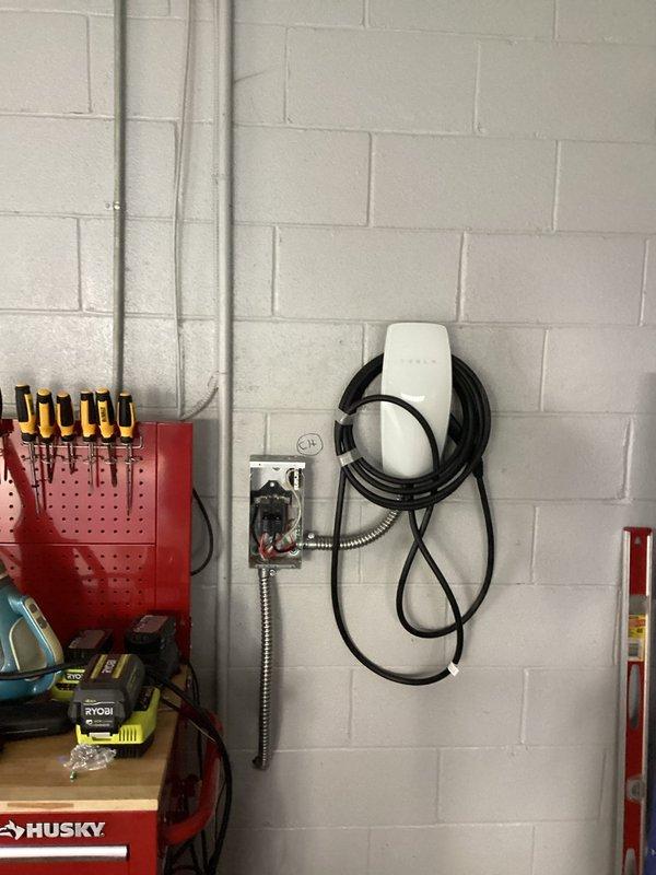 Completed 200A electrical service upgrade with full compliance to 2023 National Electrical Code requirements, including installation of required exterior disconnect. Installed dedicated EV charging circuit with appropriate conduit runs and mounted customer-supplied Tesla wall charger in garage workspace. All necessary code updates were implemented during the service upgrade, including proper grounding, bonding, and overcurrent protection. The installation features metallic conduit routing along wall surfaces to protect branch circuits, with the EV charger positioned for optimal vehicle access. All components were tested and verified operational upon completion.