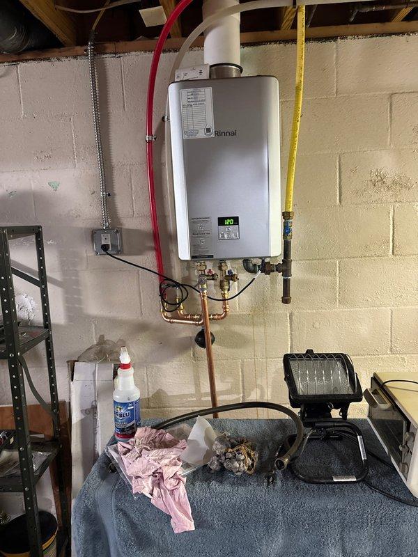 Completed tankless water heater replacement, removing existing unit and installing new Rinnai tankless system. Installation included mounting unit to wall, connecting copper water supply lines with brass shut-off valves and pressure gauge, routing PVC exhaust venting through ceiling, connecting yellow flexible gas line, and establishing electrical connections. System tested and operational at 120 degrees, with all connections verified for proper function and leak-free operation.