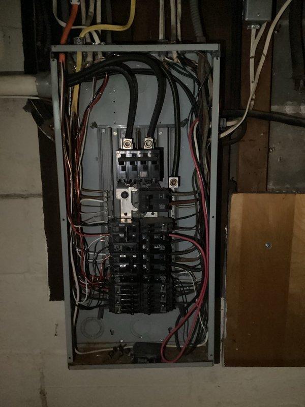 Completed electrical panel installation and circuit wiring for AC system in basement utility area. Installed main breaker panel with dual main breakers and multiple branch circuit breakers, routing and terminating multi-conductor wiring including black, red, white, and yellow conductors through organized pathways within the enclosure. Connected electrical feeds from overhead conduit runs to panel, ensuring proper wire management and code-compliant installations alongside existing HVAC ductwork and mechanical systems.