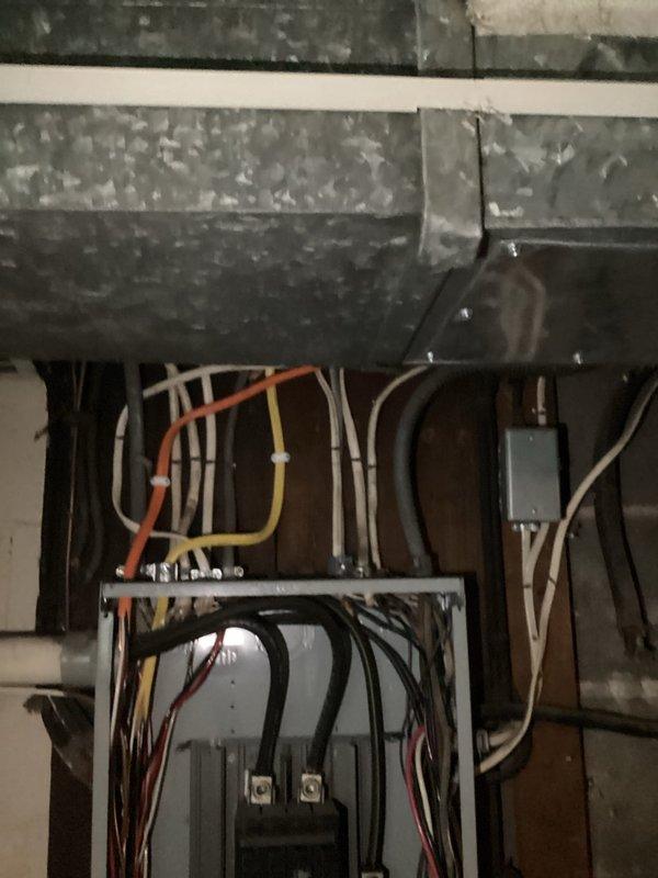 Completed electrical panel installation and circuit wiring for AC system in basement utility area. Installed main breaker panel with dual main breakers and multiple branch circuit breakers, routing and terminating multi-conductor wiring including black, red, white, and yellow conductors through organized pathways within the enclosure. Connected electrical feeds from overhead conduit runs to panel, ensuring proper wire management and code-compliant installations alongside existing HVAC ductwork and mechanical systems.