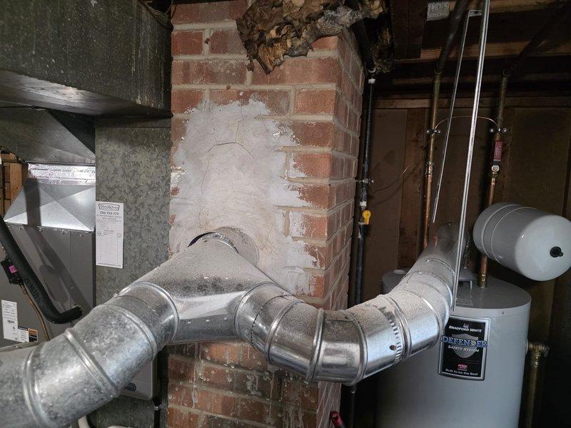 Responded to emergency service call for carbon monoxide concerns following storm damage to furnace flue stack. Upon inspection, found compromised chimney structure with damaged flue connection allowing combustion gases to backdraft into living space instead of properly venting outside. Documented existing conditions showing deteriorated brick chimney with repair patches, damaged ductwork connection to chimney, and debris at chimney crown. Assessed immediate safety hazard and coordinated timing with scheduled carbon monoxide testing. Photographed all affected areas including furnace exhaust connections, chimney structure, and venting system for insurance documentation purposes.
