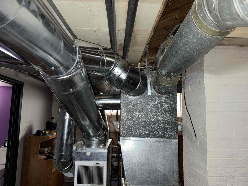 Conducted consultation and assessment of existing ductwork configuration in basement area where customer expressed concerns about low-hanging ducts interfering with ceiling clearance. Documented current HVAC system layout including Aprilaire furnace unit with extensive metallic ductwork network featuring multiple branch connections, flexible insulated ducts, and rigid metal sections. Evaluated feasibility of rerouting ductwork to achieve improved ceiling height and assessed whether mini-split system would be beneficial alternative or supplement to current forced-air setup.