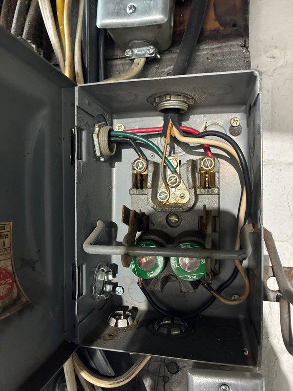 Responded to service call for electrical panel evaluation and estimate preparation. Upon arrival, inspected existing electrical service installation consisting of main breaker panel mounted on basement wall with associated junction boxes and outdated fuse panel above. Main panel appeared to be in serviceable condition with visible circuit breakers and directory labeling, though surrounding infrastructure showed age-related wear. 

Documented older fuse-style panel with screw-in fuses and brass terminal connections, noting multiple colored conductors entering the enclosure. Observed mixed vintage wiring throughout the installation with tan-colored conduits routing to ceiling area. Assessed overall electrical system configuration including panel capacity, existing circuit distribution, and connection points.

Photographed current electrical service setup to support estimate preparation for new breaker panel installation as requested. Provided customer with documentation of existing condi