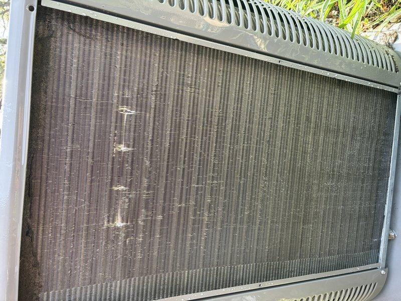 Completed scheduled MVP cooling maintenance visit on 4-year-old system. Performed comprehensive inspection of outdoor condenser unit, documenting condition of heat exchanger coils which showed moderate accumulation of dirt, debris, and environmental contamination between fins. Noted visible fin damage including bent, compressed, and corroded sections throughout coil surface, particularly in left-center areas, which may impact airflow efficiency and heat transfer performance. Captured photographic documentation of coil condition showing discoloration, staining, and minor deformation consistent with normal outdoor equipment exposure and operation.
