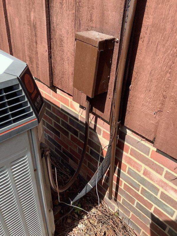 Conducted replacement estimate for a 37-year-old residential air conditioning system originally installed in 1989. Evaluated existing outdoor condensing unit with weathered electrical disconnect box and refrigerant line connections, along with indoor return air grille and distribution components. Documented current system configuration including exterior placement against brick and wood siding, electrical service connections, and interior air return installation to provide comprehensive replacement recommendations for the aging HVAC system.