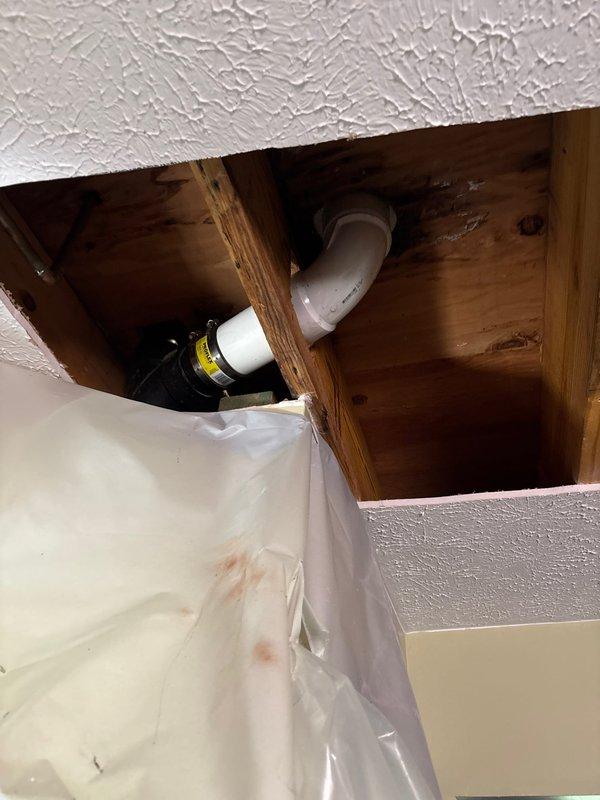 Removed existing toilet in master bathroom and extracted deteriorated toilet flange. Installed new toilet flange and mounted replacement toilet fixture to restore proper function. Accessed ceiling cavity to address water-damaged plumbing infrastructure, requiring opening of additional ceiling area for complete repair access. Coordinated with mitigation crew onsite to address water damage concerns. Inspected sump pump system and identified active leak at discharge pipe penetration point along exterior wall. Protected work areas with plastic sheeting during repair process. All replacement parts were staged and available prior to service completion.