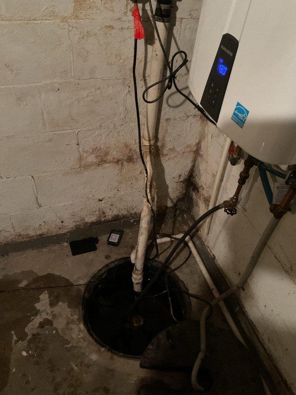 Responded to service call for non-operational sump pump with rising water levels in basement utility area. Upon arrival, inspected sump pump basin and found pump had failed, preventing proper drainage and allowing water accumulation in pit. Removed defective pump unit from basin and tested float switch mechanism, confirming mechanical failure. Installed replacement sump pump with appropriate horsepower rating for residential application. Connected discharge piping to existing white PVC vertical pipe running up wall. Verified all electrical connections were secure and properly grounded. Tested pump operation by filling basin and confirming automatic float activation and proper water discharge through existing drainage system. Pump cycled correctly and reduced water level as designed. Advised property occupant of extensive moisture damage and water staining visible on basement walls and floor, indicating history of water infiltration issues that may require additional waterproofing measu