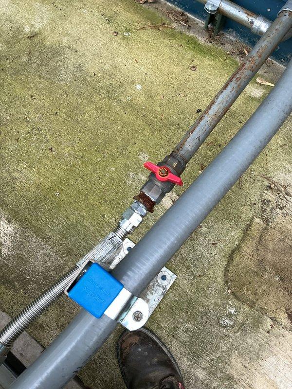 Responded to report of natural gas odor detected near 3-year-old generator unit. Upon inspection, identified corroded gas line connections at the flex connector coupling point where the rigid pipe meets the flexible metal conduit supplying the generator. The threaded metal fittings showed significant rust deterioration and weathering from outdoor exposure, which compromised the integrity of the gas line connection. Documented the corroded components and deteriorated mounting hardware with photographic evidence showing the extent of rust damage on the vertical supply pipe, valve assembly, and coupling connections. The installation showed signs of prolonged moisture exposure with biological growth on surrounding surfaces, contributing to accelerated corrosion of the gas line components.
