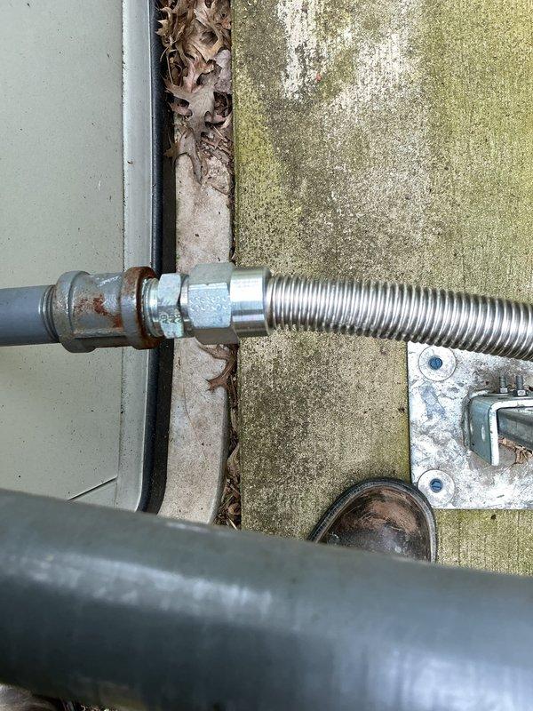Responded to report of natural gas odor detected near 3-year-old generator unit. Upon inspection, identified corroded gas line connections at the flex connector coupling point where the rigid pipe meets the flexible metal conduit supplying the generator. The threaded metal fittings showed significant rust deterioration and weathering from outdoor exposure, which compromised the integrity of the gas line connection. Documented the corroded components and deteriorated mounting hardware with photographic evidence showing the extent of rust damage on the vertical supply pipe, valve assembly, and coupling connections. The installation showed signs of prolonged moisture exposure with biological growth on surrounding surfaces, contributing to accelerated corrosion of the gas line components.